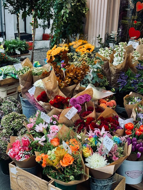 A vibrant display of freshly arranged flower bouquets in a florist shop window, featuring a variety of blooms including bright yellow sunflowers, pink lilies, red roses, purple and white carnations, a